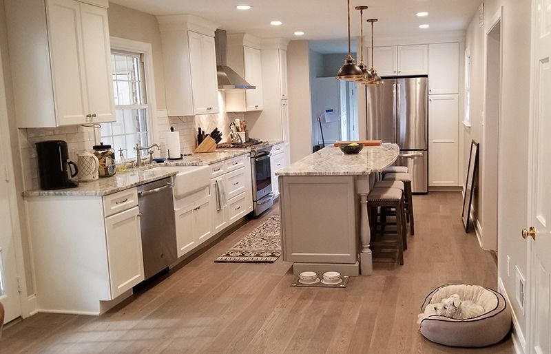 Bright white kitchen with light wood floors, stainless steel appliances, and a gray island with seating.