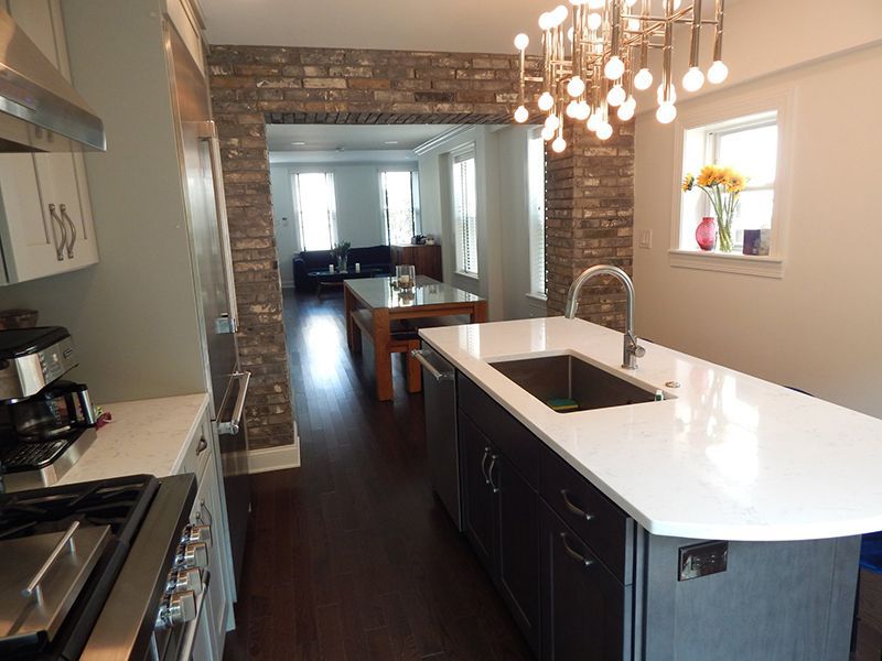 Kitchen with island and stainless steel appliances; exposed brick archway leads to dining and living areas.