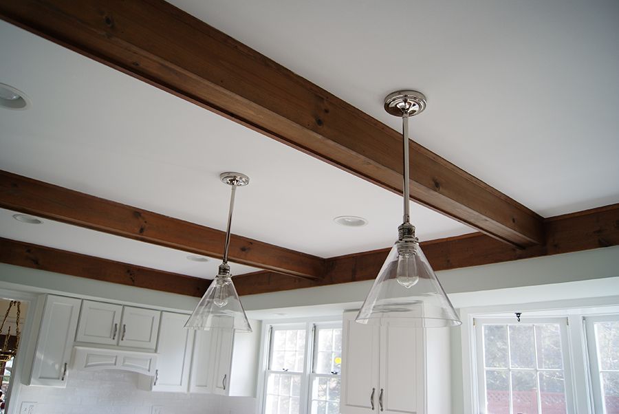 Kitchen ceiling with wooden beams, white cabinets, and two clear glass pendant lights.