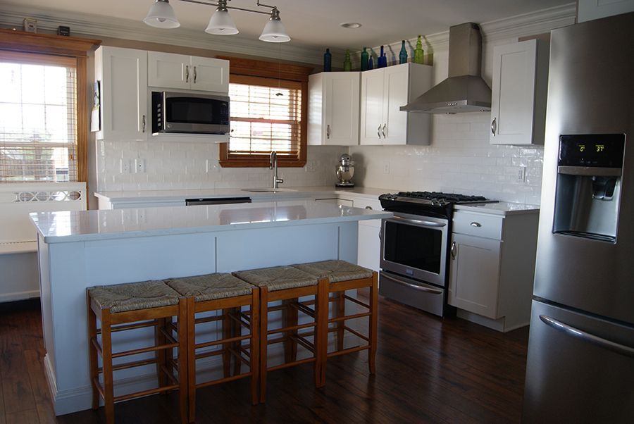 White kitchen with stainless steel appliances, white cabinets, and wooden stools at the island.