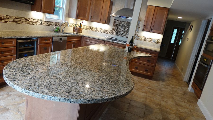 Kitchen with granite countertop island, brown cabinets, tile backsplash, stainless steel appliances.