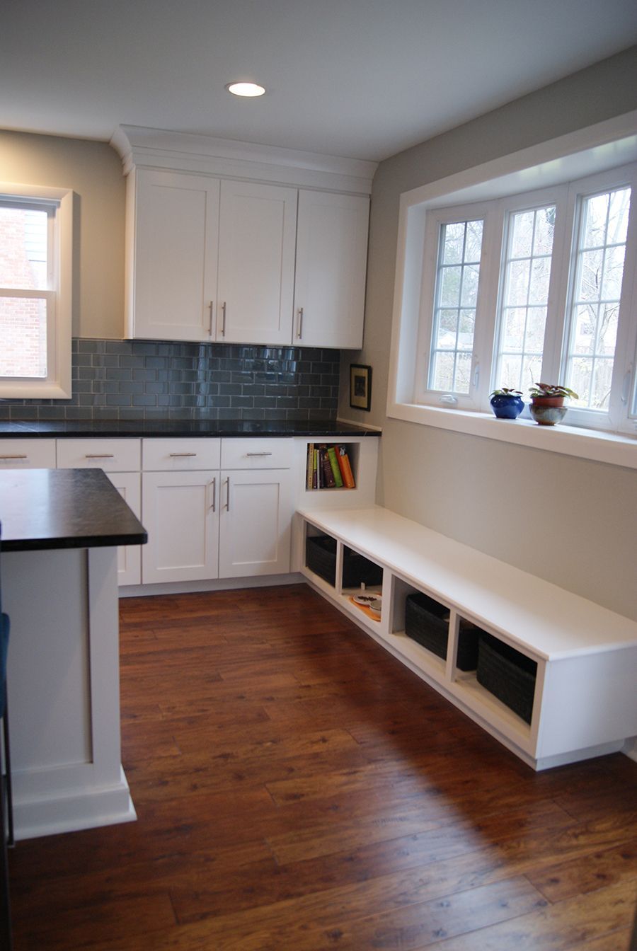Kitchen with white cabinets, black countertop, blue tile backsplash, and built-in bench under a window.