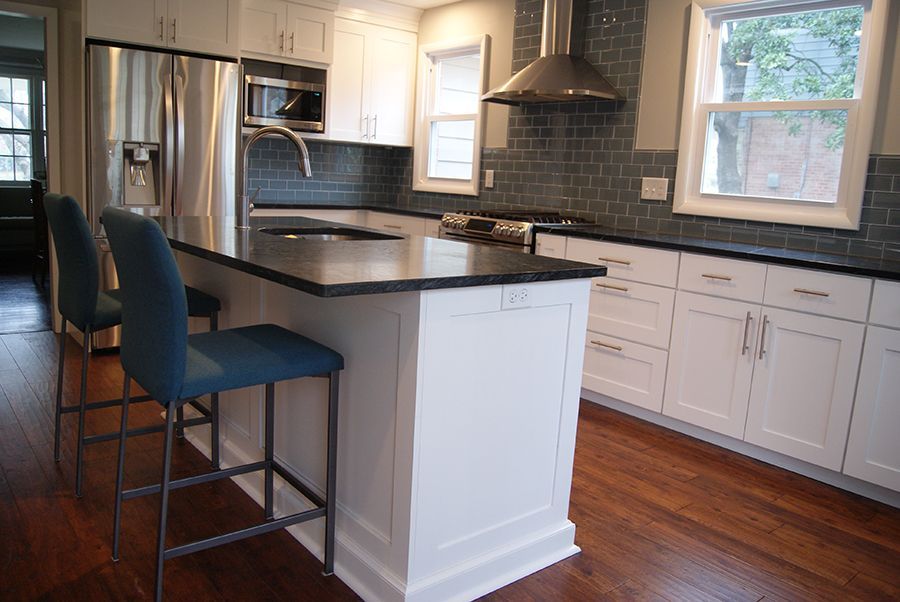 Modern kitchen with white cabinets, dark countertops, island with seating, and stainless steel appliances.