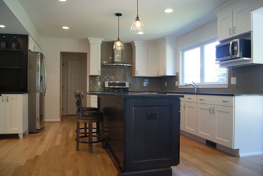 Modern kitchen with white cabinets, dark island, and stainless steel appliances.