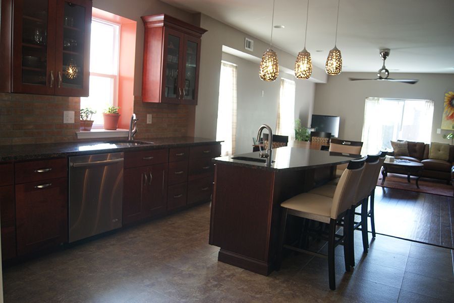 Kitchen with dark wood cabinets, stainless steel appliances, island with stools, and open to a living area.