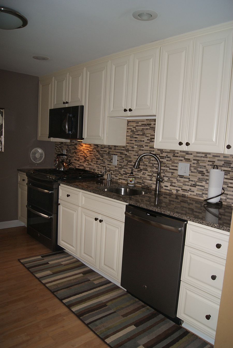 Cream-colored kitchen cabinets and appliances with dark countertops and a mosaic tile backsplash.