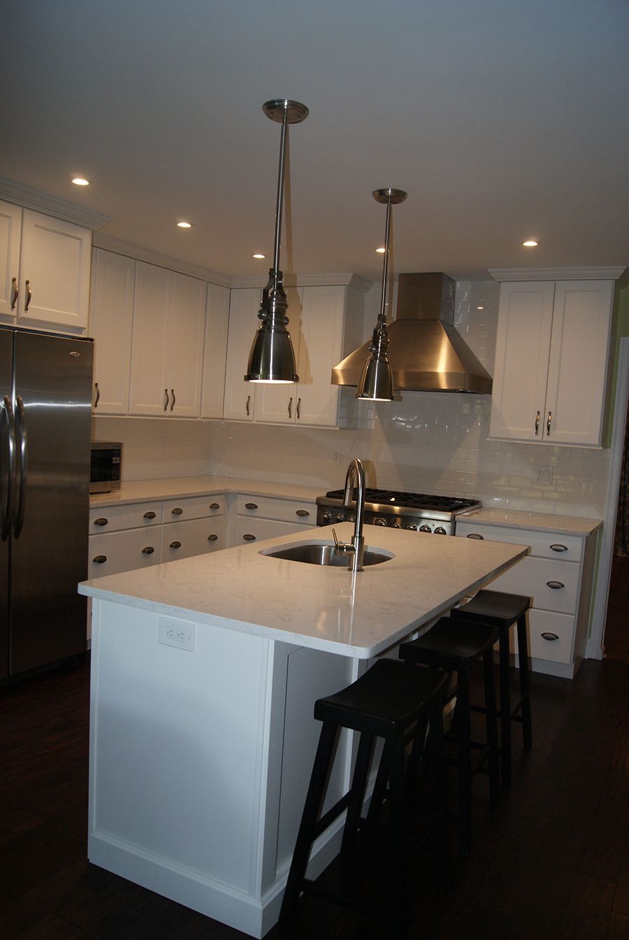 White kitchen with island, stainless steel appliances, pendant lights, and black stools.