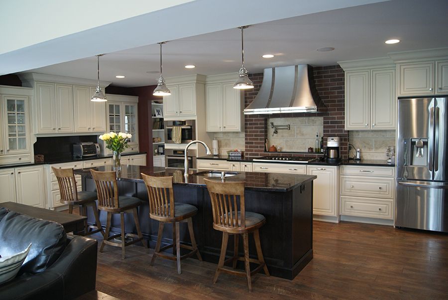 Spacious white kitchen with dark island, stools, stainless steel appliances, and exposed brick behind the range.