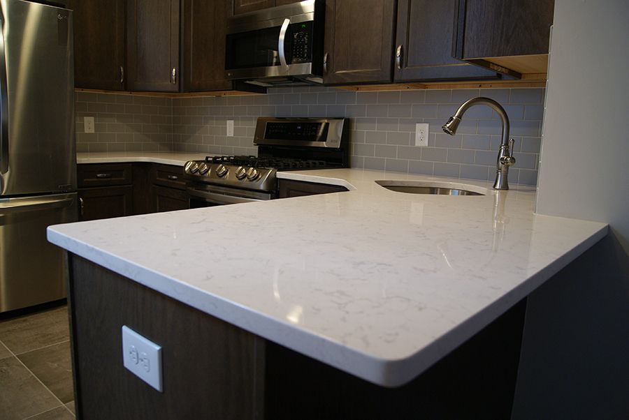 Kitchen with white countertop, stainless steel appliances, dark cabinets, and tile backsplash.