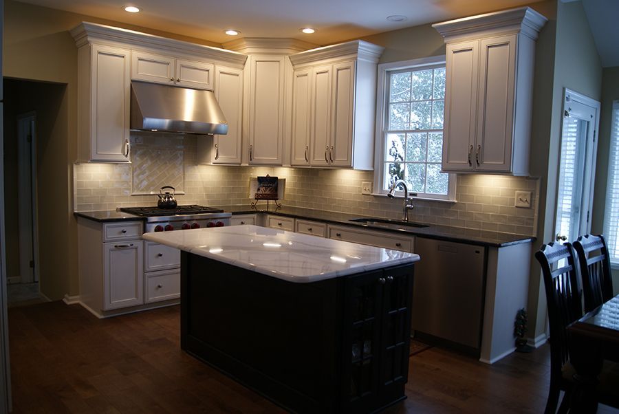 Kitchen with white cabinets, dark island, stainless steel appliances, and wood floors.