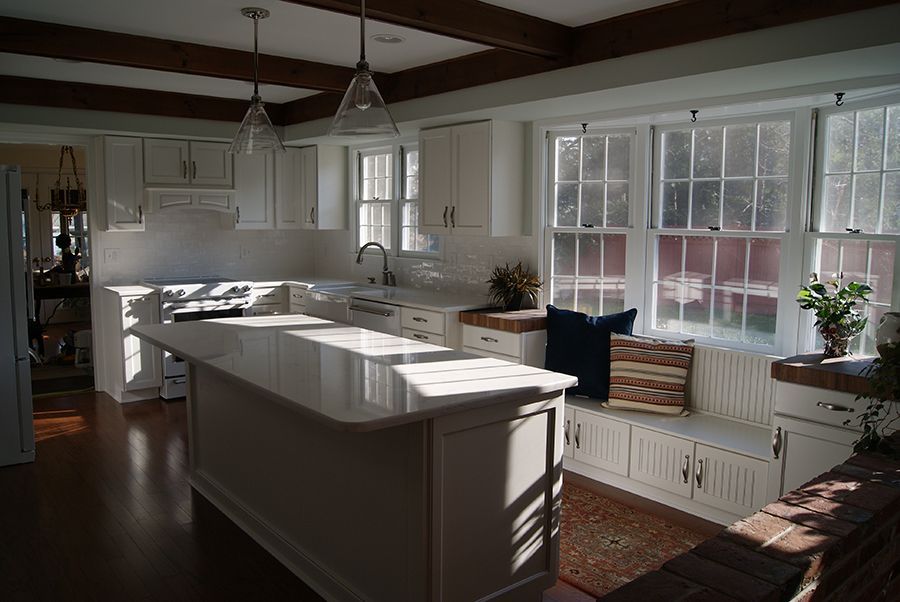 Bright white kitchen with island, wooden beams, large windows, and built-in bench.