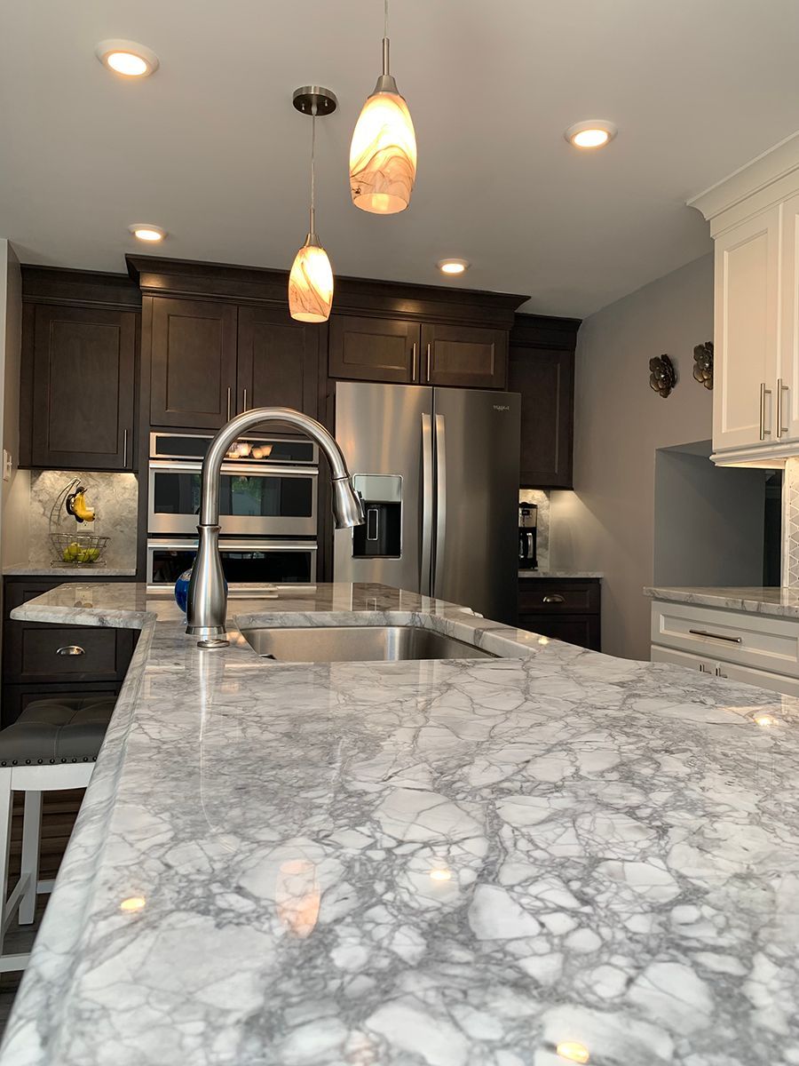 Kitchen with marble countertop, stainless steel appliances, dark brown and white cabinets, and pendant lights.