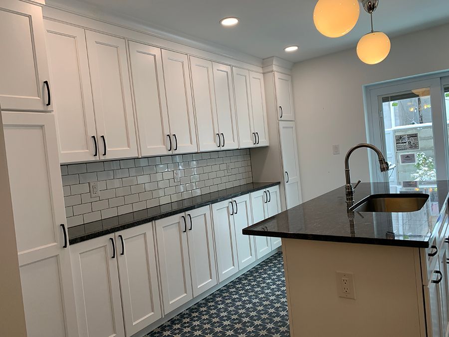 White kitchen cabinets and island with black countertops, sink, and backsplash.