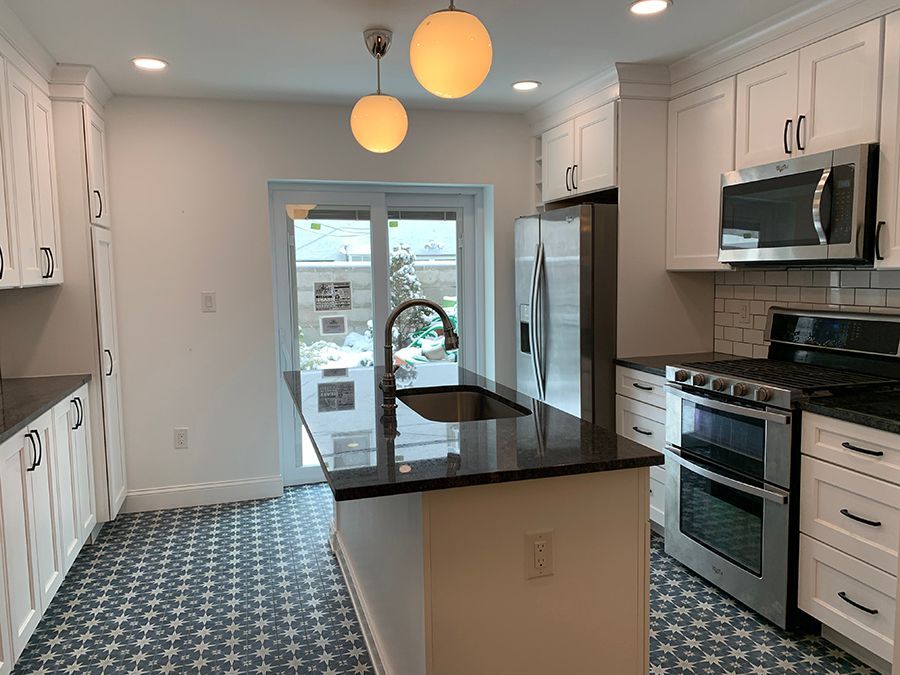 White kitchen with a black countertop island, stainless steel appliances, and patterned blue floor tiles.