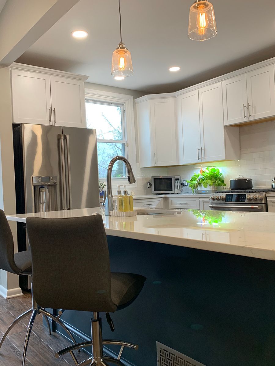 Modern kitchen with white cabinets, blue island, stainless steel appliances, and pendant lights.