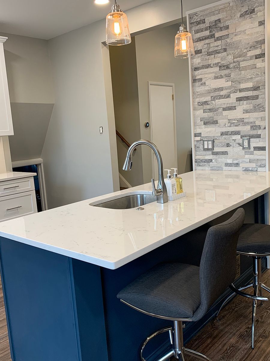 Modern kitchen island with white countertop, dark blue base, and two gray bar stools.