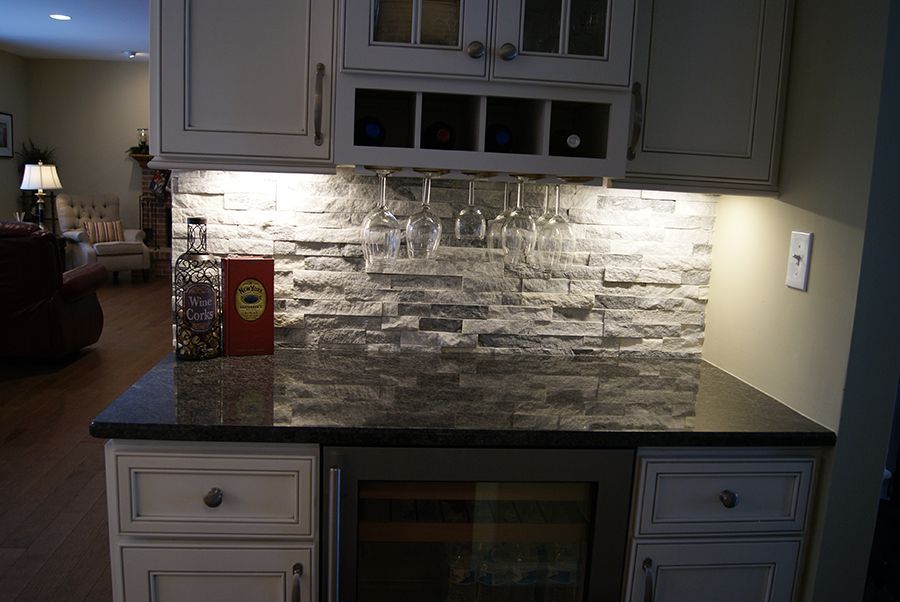 Bar area with white cabinets, stone backsplash, wine glasses, and a wine cooler.
