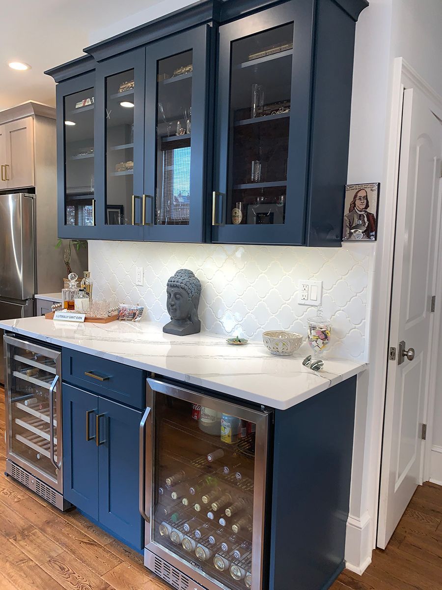 Navy blue bar cabinet with glass-fronted upper cabinets, wine fridges, white countertop, and Buddha statue.
