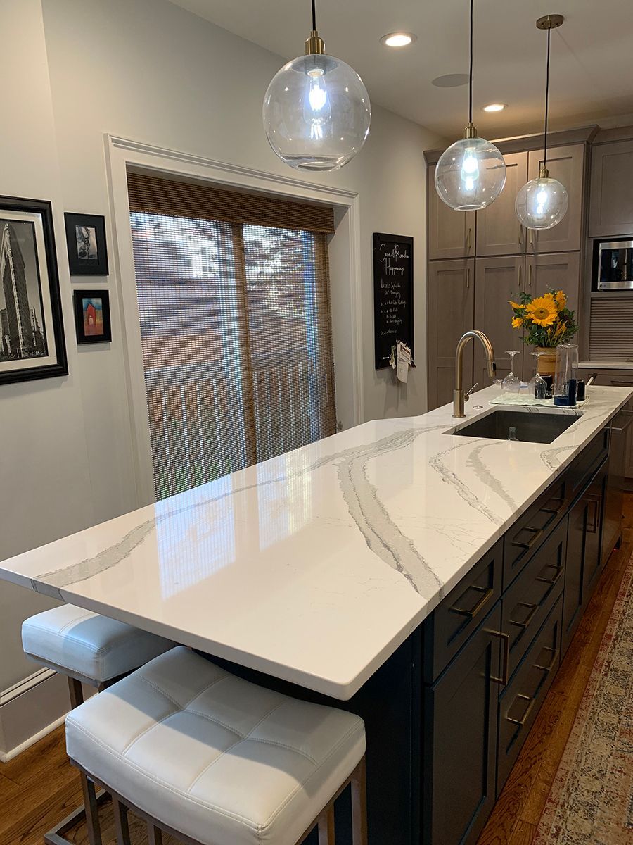Modern kitchen island with white countertop, dark cabinets, and clear globe pendant lights.