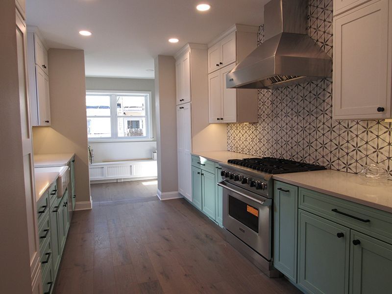 Modern kitchen with mint green and white cabinets, stainless steel appliances, and patterned backsplash.