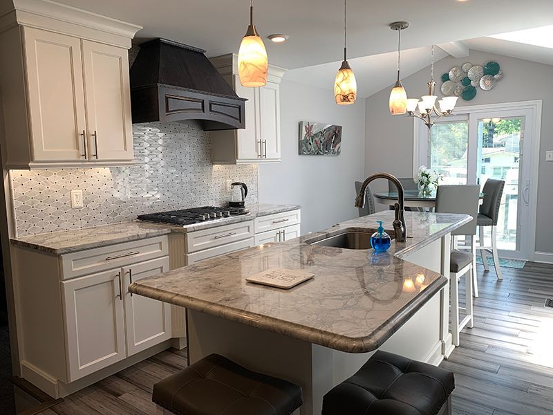 White kitchen with island, gray countertops, and wood flooring. Pendant lights hang above.