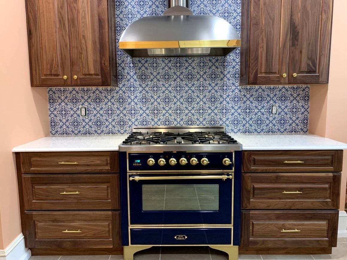 Kitchen with blue oven, wooden cabinets, patterned backsplash, and stainless steel hood.