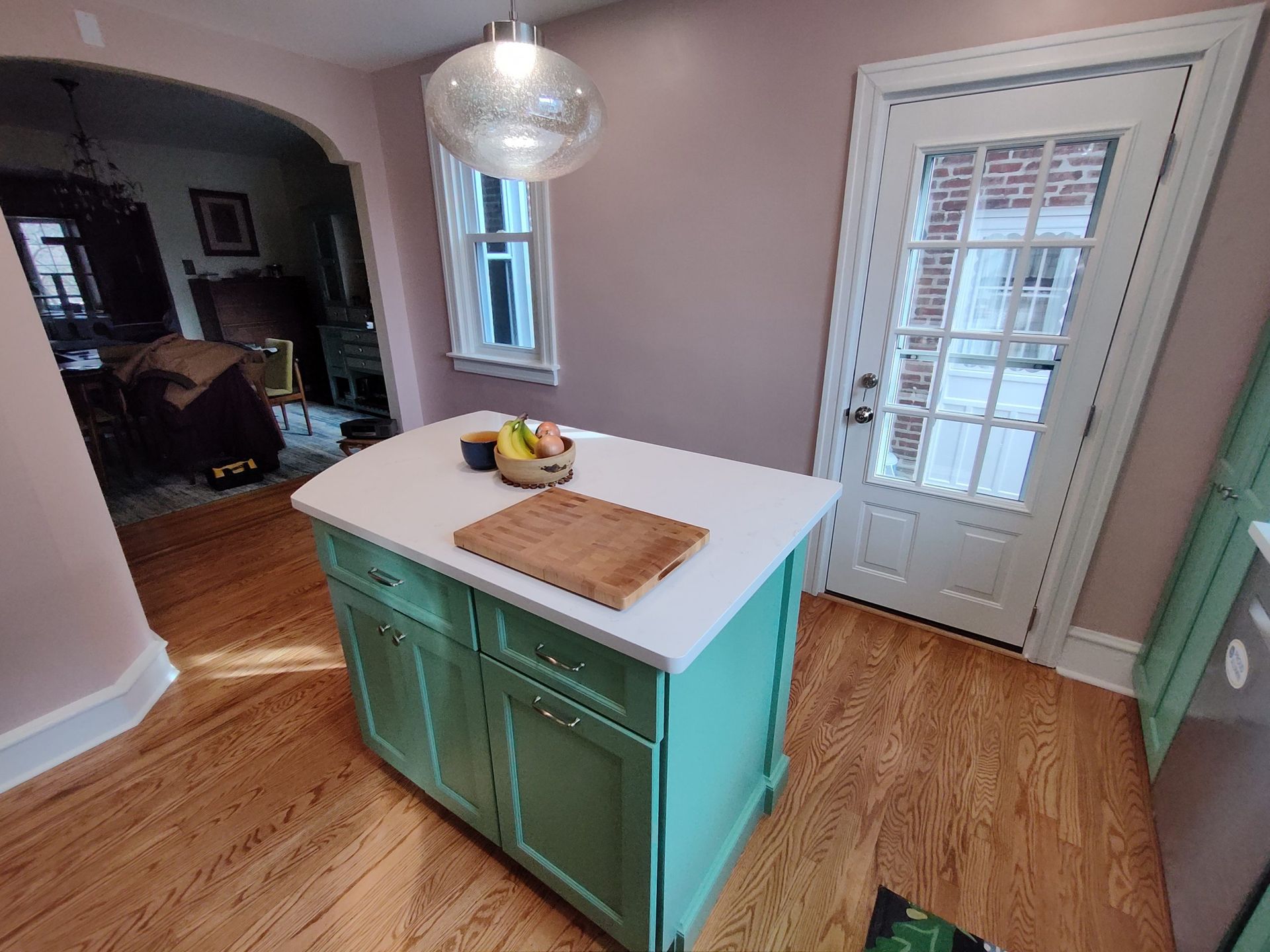 Kitchen with turquoise island, white countertop, wooden floor, glass door, and pale pink walls.