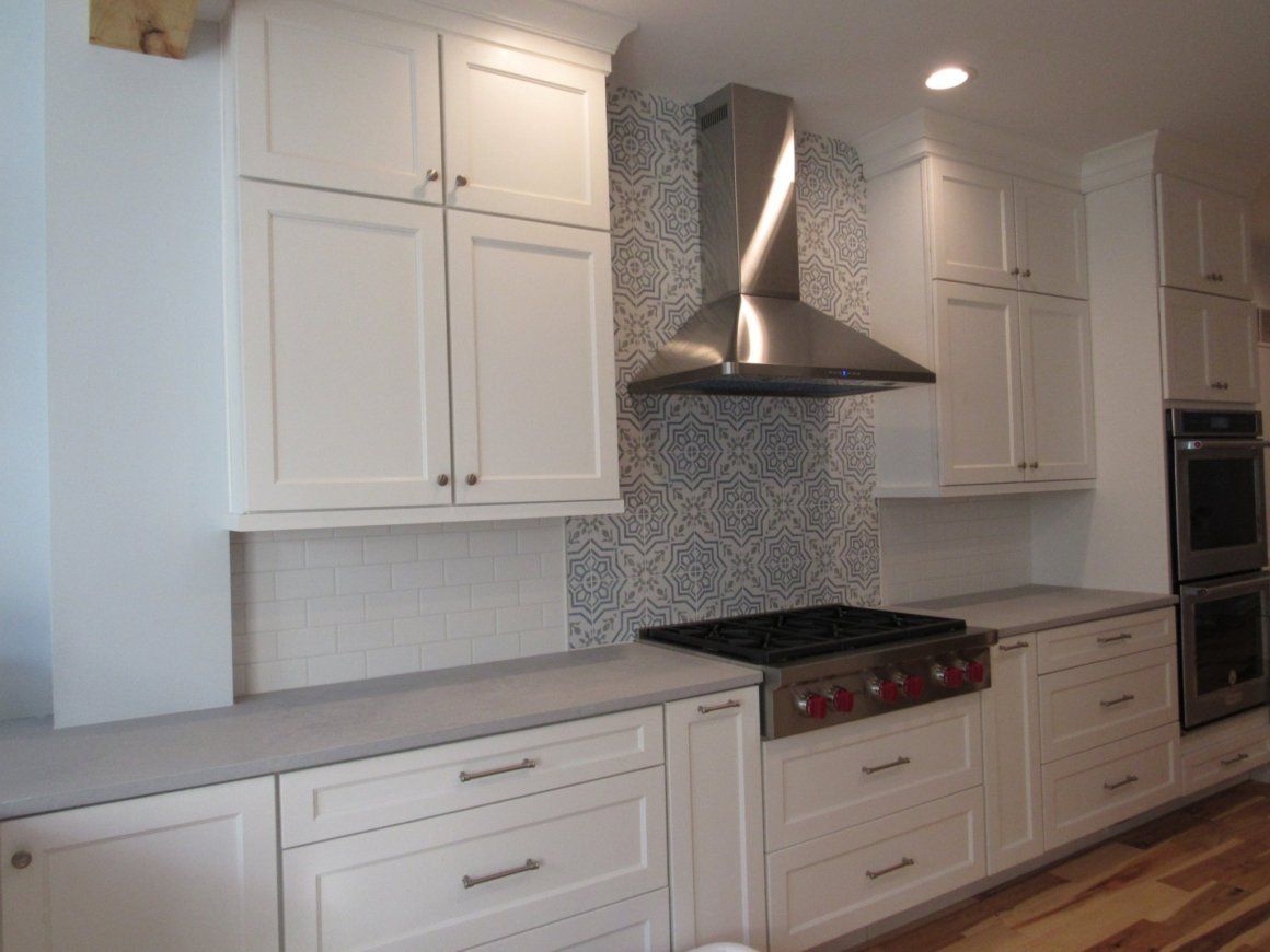 White kitchen cabinets with gray countertops, stainless steel range hood, and patterned backsplash.