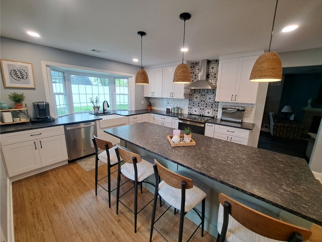 Modern kitchen with white cabinets, gray countertops, island with bar stools, and pendant lights.