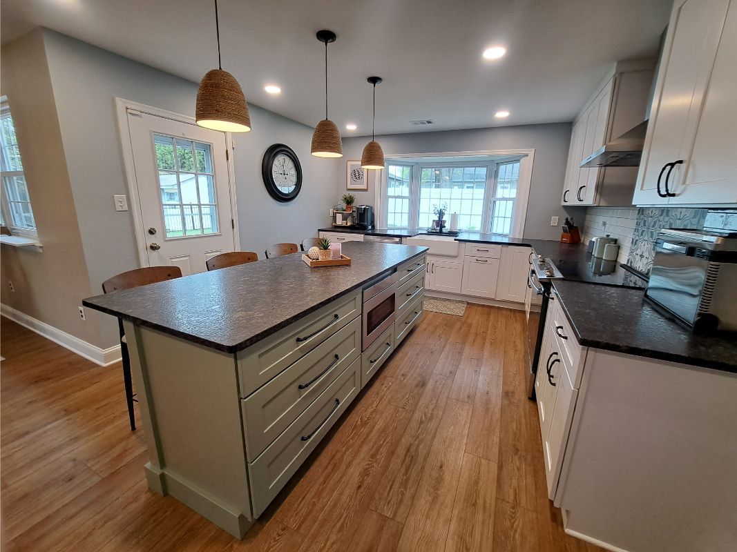 Kitchen with large island, white cabinets, dark countertops, wood floors, and pendant lights.