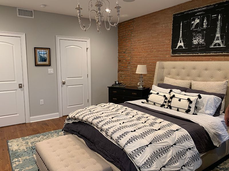 Bedroom with exposed brick accent wall, tufted headboard bed, and chandelier.