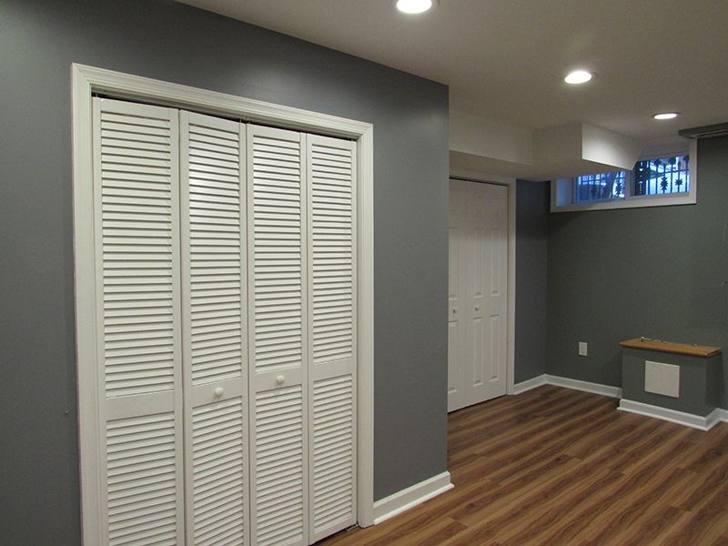 Gray-painted room with white closet doors and laminate flooring. Recessed ceiling lights and a small window are visible.