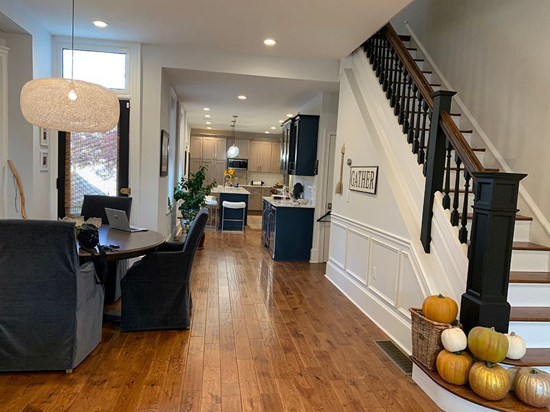 A bright interior of a home with dining, kitchen, and stairwell. Pumpkins sit on the stairs.