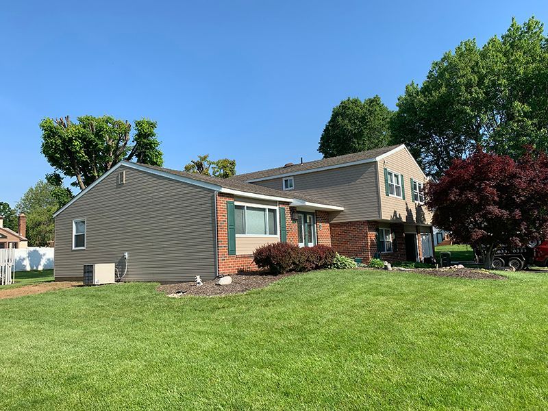 Two-story house with green shutters, brick facade, and gray siding on a sunny day.