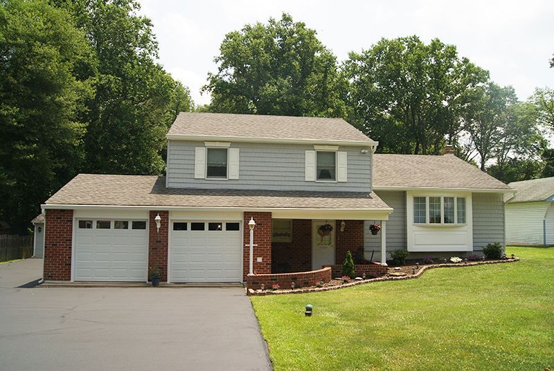 Two-story gray house with white garage doors and a manicured lawn.