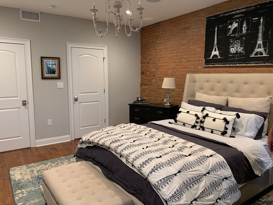 Bedroom with exposed brick wall, bed with white and blue bedding, and a chandelier.