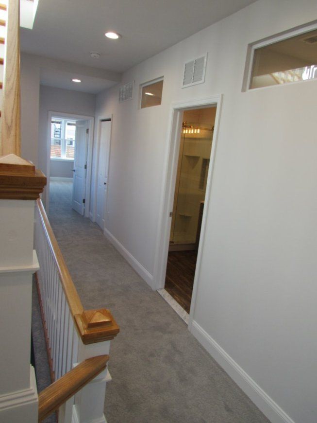 Hallway with gray carpet, white walls, closed doors, and a bathroom doorway with a partial view.