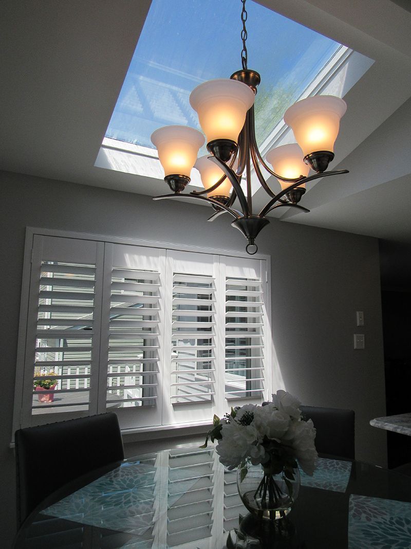 Dining room with chandelier, skylight, window with white shutters, table with flowers.