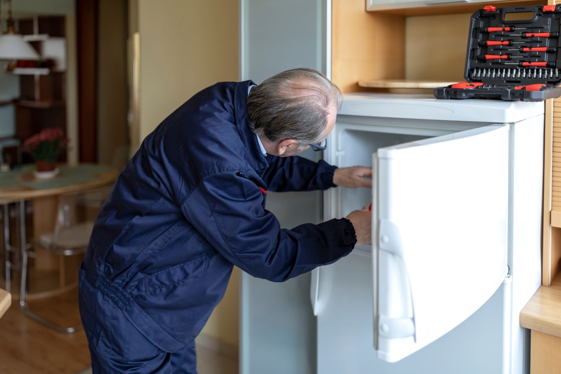 A man is fixing a refrigerator in a kitchen. - Memphis, TN - Repair Squad Home Service