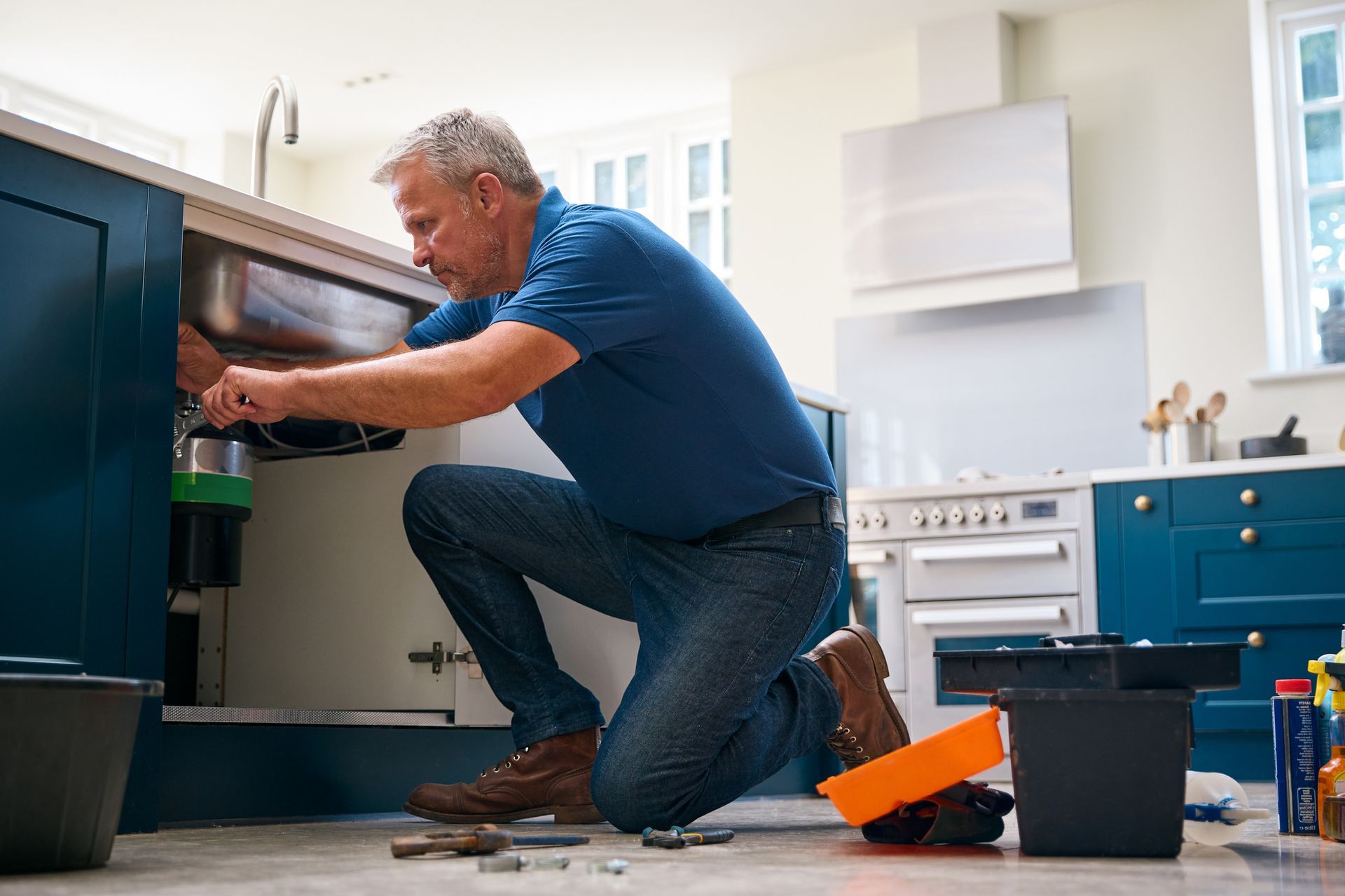 A man is kneeling down in a kitchen fixing a sink. - Memphis, TN - Repair Squad Home Service