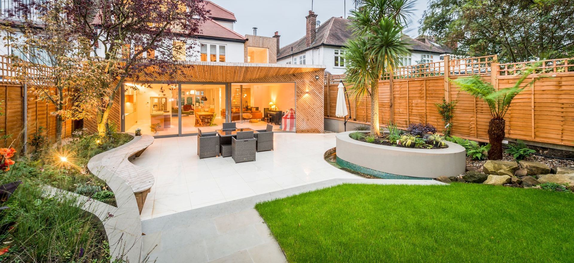 Un jardin moderne avec une terrasse, une pelouse et un coin salon devant la maison.