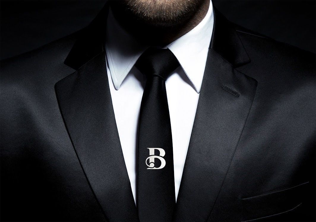 A man in a suit and tie with the letter b on his tie clip