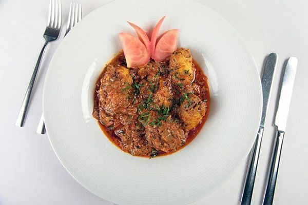 A white plate topped with a stew of meat and potatoes next to silverware.