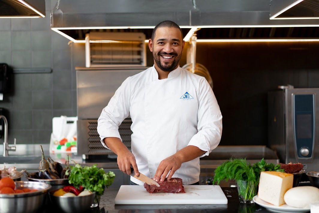 A chef is cutting a piece of meat on a cutting board in a kitchen.