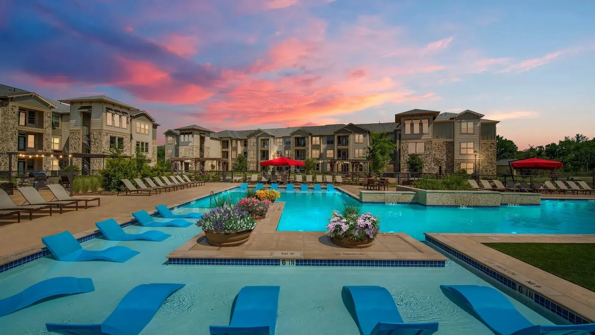 Swimming pool area with lounge chairs and flowers at sunset