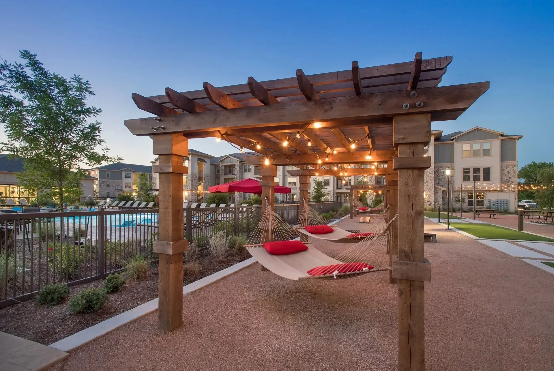 Outdoor hammocks under wooden structure with lights near a pool area.