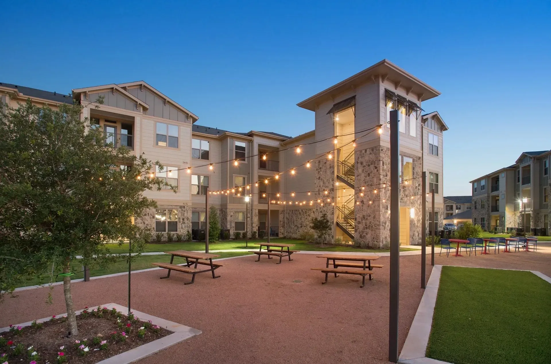 Outdoor area with picnic benches, landscaping, and twinkling lights in a multi-unit residential property.