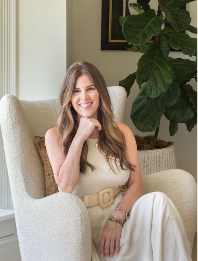 A woman in a white dress is sitting in a chair and smiling.