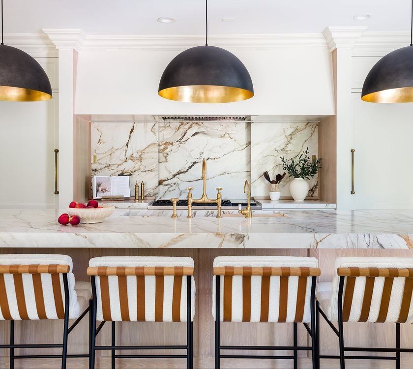 A kitchen with a marble counter top and striped bar stools