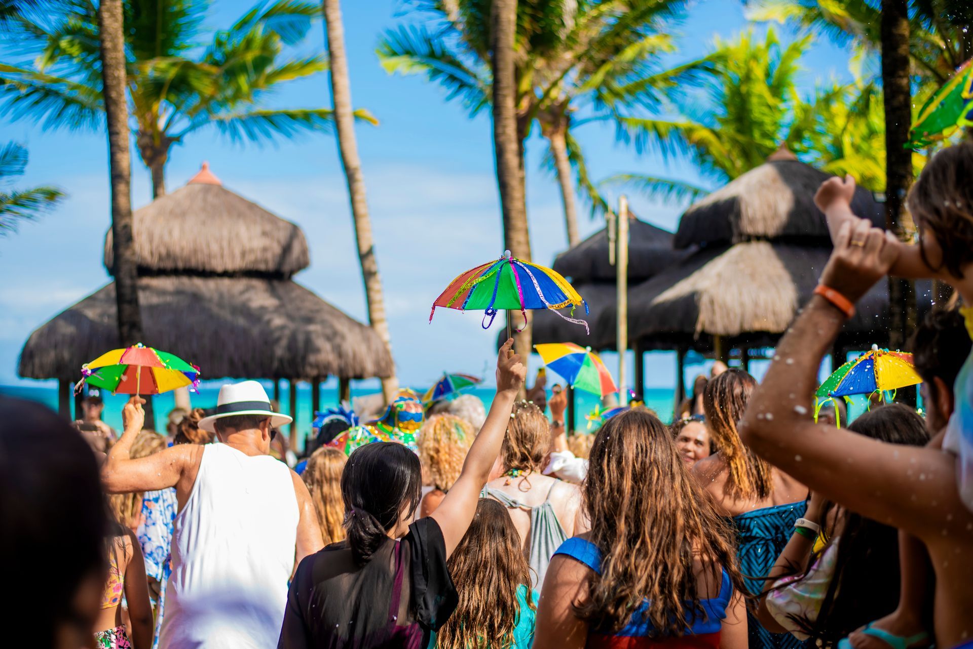 Uma multidão de pessoas está em uma praia segurando guarda-sóis coloridos.